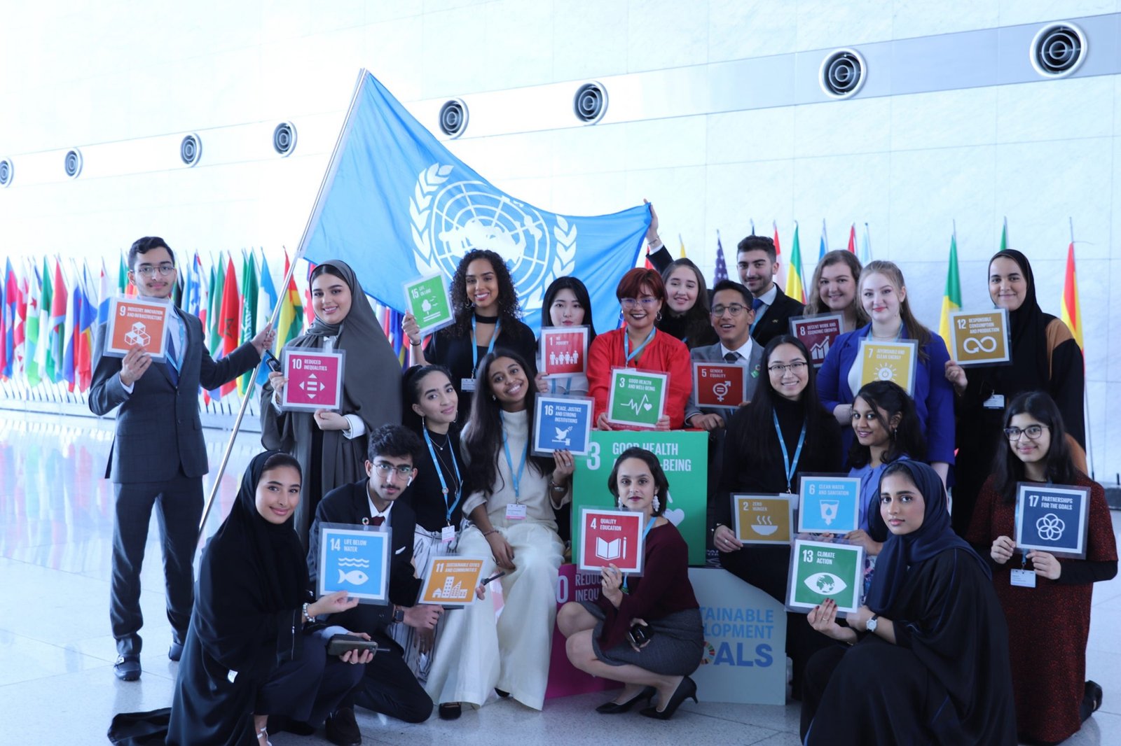 Doha MUN delegates standing together beneath the United Nations flag, each holding a placard for one of the seventeen Sustainable Development Goals.