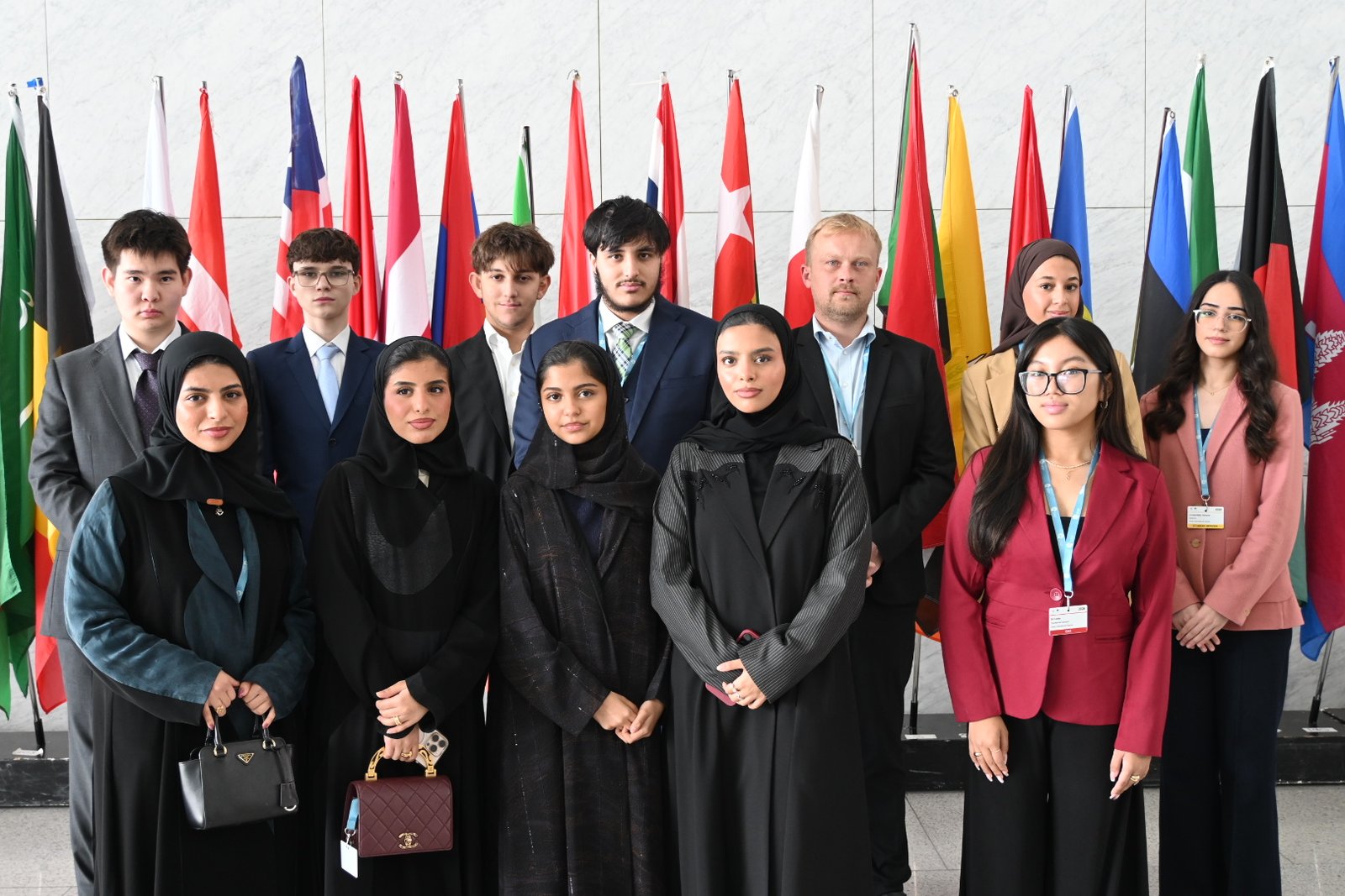 Delegates standing before the row of national flags in the atrium at Doha MUN 2026.